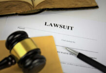 A gavel resting on a legal document titled 'LAWSUIT' with a pen and an open book in the background