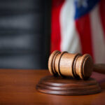 Jury Clash Explodes Weinstein Rape Trial A wooden gavel resting on a round base with a blurred American flag in the background