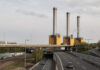 Regulators on Edge: $400 Billion Power Merger Industrial power plant with three tall smokestacks beside a highway