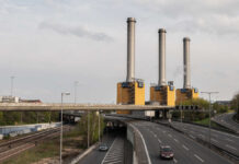 Industrial power plant with three tall smokestacks beside a highway