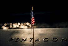 A small American flag positioned in front of the word 'PENTAGON' on a reflective surface