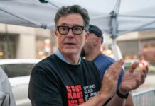Colbert Era ENDS: CBS Shuts Down Iconic Show A man in a black t-shirt with a writers' guild logo clapping at a public event