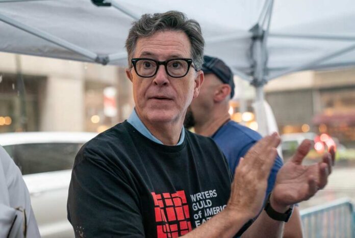 Stephen,Colbert,Serves,Ice,Cream,To,Striking,Members,Of,Writers A man in a black t-shirt with a writers' guild logo clapping at a public event
