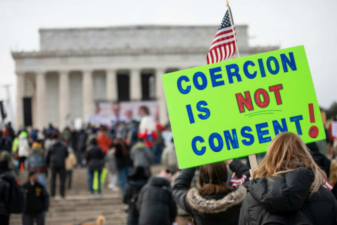 A crowd at a protest with a sign reading COERCION IS NOT CONSENT! in front of the Lincoln Memorial