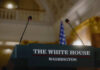Press podium with microphones and an American flag in the background