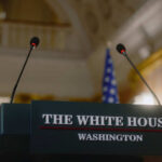 US-Only AI Rollout Sparks Control Fight Press podium with microphones and an American flag in the background