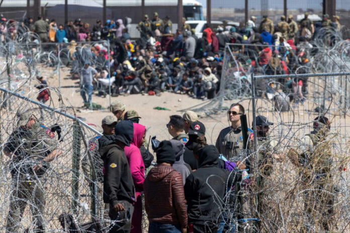 shutterstock2497167437jpg A crowd of people at a border area with law enforcement and barbed wire