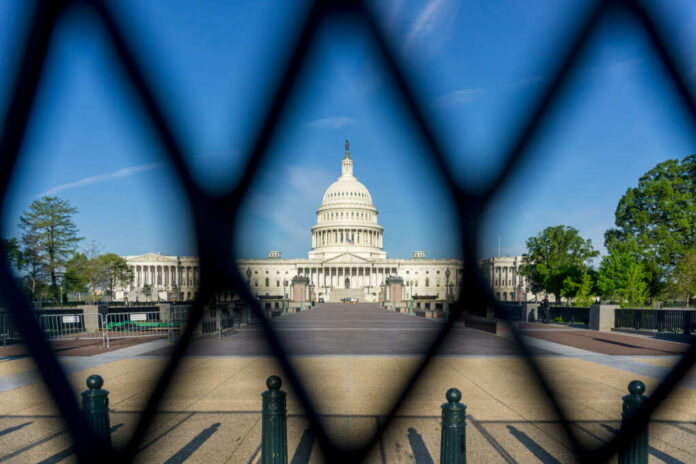 shutterstock_1959169297 View of the U.S. Capitol building through a security fence