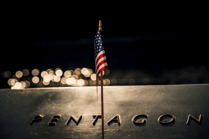Close-up,Of,An,American,Flag,Draped,Across,The,Iconic,Pentagon A small American flag positioned in front of the word 'PENTAGON' on a reflective surface