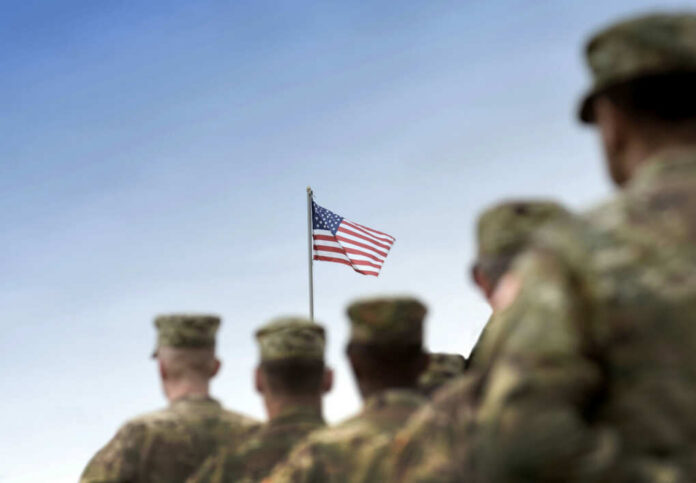 shutterstock_2380883205 Soldiers in uniform standing in formation with an American flag in the background