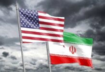 Flags of the United States and Iran waving against a cloudy sky