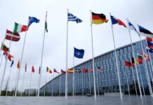 22 Nations Warn Iran: Hands Off Our Soil Flags of various countries in front of a modern building under a cloudy sky