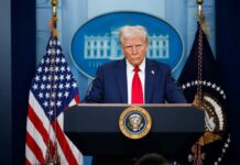A political figure at a podium during a press conference in front of the White House