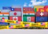 Stacked shipping containers with national flags behind yellow tariffs tape
