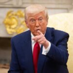 Trump Promises Payback Over ‘Rigged’ 2020 A man in a blue suit and red tie pointing while seated