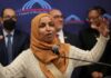 A woman in a hijab passionately speaking at a podium during a public event