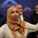 Go Back Blast Ignites Minnesota Firestorm A woman in a hijab passionately speaking at a podium during a public event