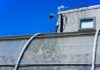 Grooming Gang Bombshell — Who Hid This? Security camera mounted above a prison fence with barbed wire against a blue sky
