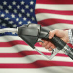 A hand holding a fuel pump in front of an American flag