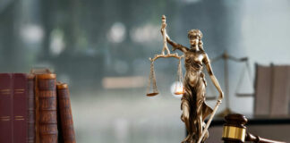 A bronze statue of Lady Justice holding scales and a sword, with law books and a gavel in the foreground