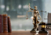 A bronze statue of Lady Justice holding scales and a sword, with law books and a gavel in the foreground