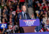 SHOCKING Crackdown Targets Protest Networks A speaker addressing a crowd at a political rally with campaign signs and flags in the background