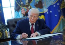 Trump’s Monument Speedway Sparks Fury A person in a suit signing documents at a desk in the Oval Office