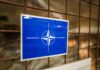 NATO emblem on a blue sign attached to a rusty wire fence