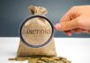 hand holding magnifying glass over burlap money bag with coins