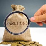 hand holding magnifying glass over burlap money bag with coins
