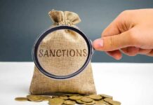 hand holding magnifying glass over burlap money bag with coins