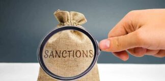 hand holding magnifying glass over burlap money bag with coins