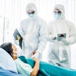 Ebola Outbreak Surges — Cash Scramble Intensifies Healthcare workers in full PPE attending to a hospital patient