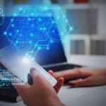 Hands using smartphone near laptop with digital hexagon interface overlay