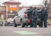 Police officers gather beside a patrol SUV at a taped-off scene