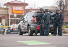Police officers gather beside a patrol SUV at a taped-off scene