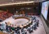 Delegates seated around a circular conference table in a large chamber