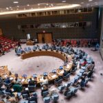 Delegates seated around a circular conference table in a large chamber