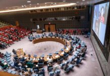 Delegates seated around a circular conference table in a large chamber