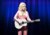 Singer in pink outfit playing a glittery acoustic guitar on stage