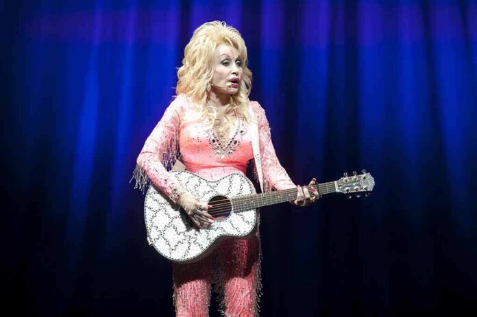 Singer in pink outfit playing a glittery acoustic guitar on stage