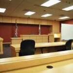 Outrage Erupts: Killer Walks Early Interior view of an empty courtroom with wooden furniture and American flags