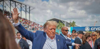 Donald Trump waving while walking through a crowded outdoor event