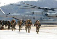 Soldiers disembark and walk past a large military helicopter