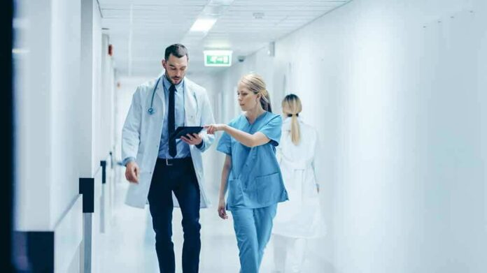 shutterstock_1189798168 Doctor and nurse walking in a hospital corridor reviewing a tablet