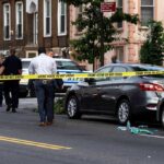 Police at urban street crime scene with yellow tape around parked cars