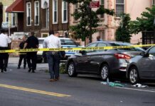 Police at urban street crime scene with yellow tape around parked cars