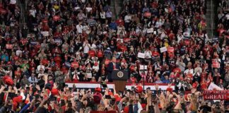 Speaker at podium addressing large crowd in arena