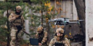 Quadcopter drone flying near camouflaged soldiers outdoors