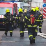 Firefighters walking toward a scene with hoses and a red emergency van